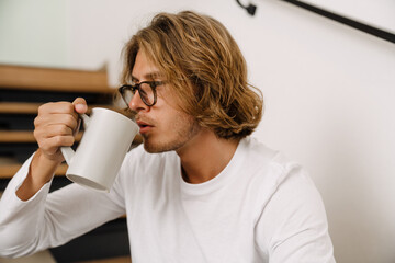 White young man sitting on stairs at home and drinking coffee