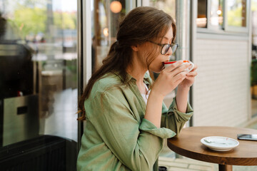 Young beautiful woman in glasses drinking coffee sitting at cafe