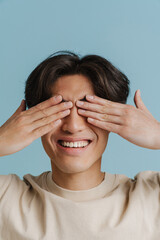 Young handsome smiling asian boy covering his eyes with hands
