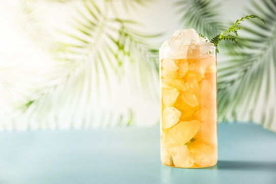 iced tea with crashed ice in a transparent tall glass on tropical background with leaves, space for text or promo