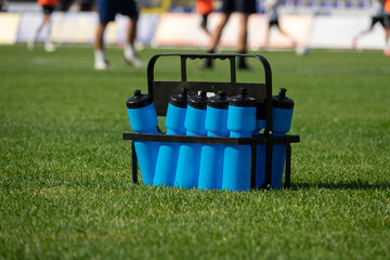 Sport bottles of fresh water or energy drink on asoccer, football field