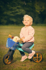 One and half year old baby girl on tricycle bike with ferret friend