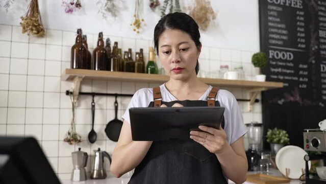 concentrated asian beverage shop owner providing online food delivery service is checking orders from customers on the electronic pad