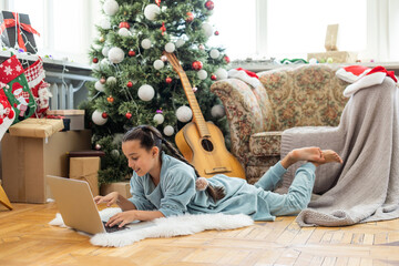 winter holidays, technology and children concept - little student girl with laptop computer at home over christmas tree background.