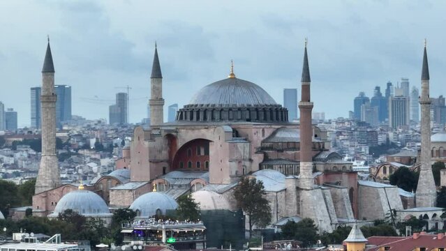 Establishing orbiting aerial drone shot of a Hagia Sophia Holy Grand Mosque with Bosphorus bridge and city skyline with a flag on the background in Fatih, Istanbul, Turkey at sunset.