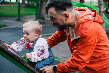 dad plays with his little daughter in a beautiful Ukrainian embroidered shirt on the playground on a sunny day