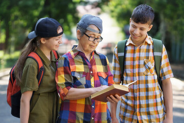 portrait of students and a teacher in a city park, teenage schoolchildren a boy and a girl are standing on the path and discussing lessons with a educator, reading a book and talking