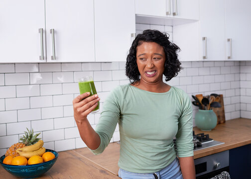A young multiracial woman pulls a face at nasty tasting green smoothie