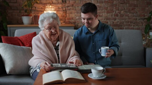 Grandmother showing old photos to her grandson with Down syndrome at home.