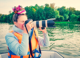 A middle-aged woman with a fancy hairstyle holding a takes pictures of landscapes with a large professional camera. Adventure and Travel on water concept.