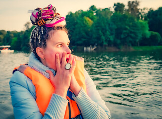 Middle aged woman with fancy hair wearing nautical lifejacket scared and amazed with open mouth for surprise, shocked face. Frightened girl at the lake