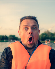 Middle aged handsome man wearing nautical lifejacket afraid and shocked with surprise expression, fear and excited face on lake background.