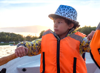 Happy boy brunette 9 years old in a life jacket while walking on a boat. Fun holidays with paddles on the lake