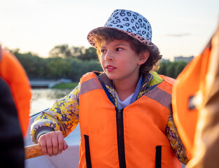 Happy boy brunette 9 years old in a life jacket while walking on a boat. Fun holidays with paddles...