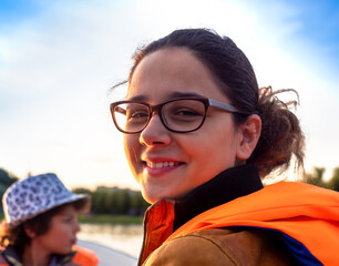 Beautiful brunette woman teen with glasses and in an orange life jacket rowing oars while sitting in a boat. Family walks at the boat station