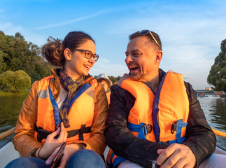 daughter teenager on boat with dad in life jackets in summer on lake. Family having fun laughing