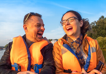 daughter teenager on boat with dad in life jackets in summer on lake. Family having fun laughing