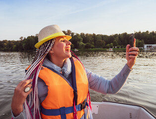 Woman taking picture of herself on smartphone during floating on kayak. Concept of rest, leisure and weekend. Middle Age Woman wearing life vests. Sunny autumn daytime.selective focus