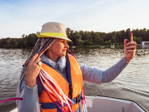 Woman taking picture of herself on smartphone during floating on kayak. Concept of rest, leisure and weekend. Middle Age Woman wearing life vests. Sunny autumn daytime.selective focus