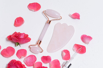 Pink guasha massager and serum lie on a white background with rose petals. beauty and salon facial theme