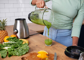 Close up of woman pouring homemade green smoothie into glass