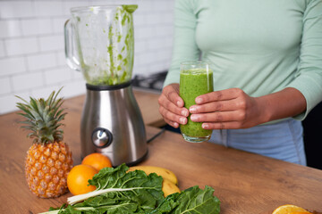 Close up of a young woman holding freshly made green smoothie at home