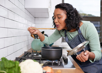 A young multi-racial woman smells and tastes her cooking on the stove