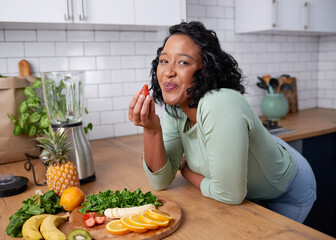 A young attractive woman tastes a strawberry while preparing fruit for smoothie