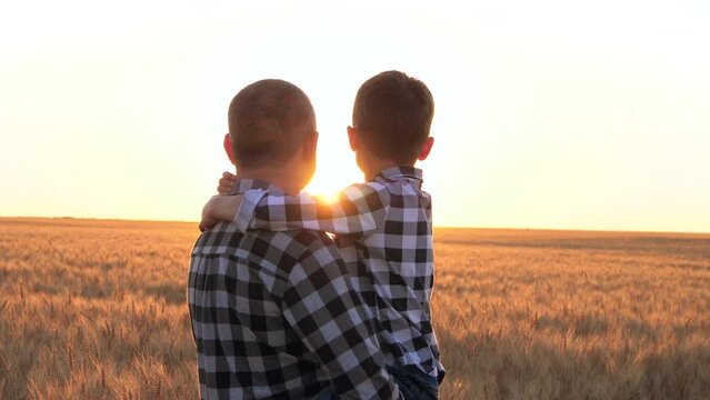 The son hugs his dad. Happy family in the sun. Father and son watch the sunset on a wheat field. The concept of a family business. Father's Day