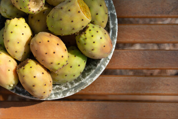 Several ripe prickly pear fruits lie in a ceramic bowl. The bowl stands on a base made of rustic wood. There is space for text.