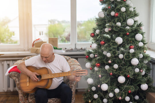 Happy people family concept - Old senior man enjoying the guitar on the sofa in the house at christmas