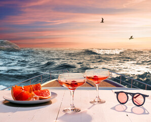 Romantic evening sea trip. Cocktail glasses, fruit on deck of private yacht during honeymoon holidays, outdoors. Love, travel, vivid impressions