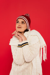 Dreamy woman in hat and knitted scarf looking away isolated on red.