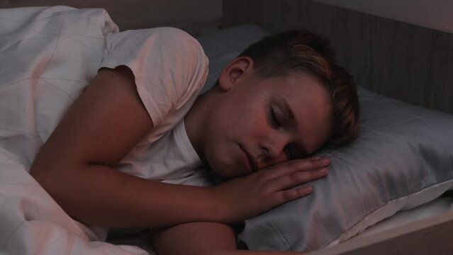 A cute schoolboy sleeps peacefully in a comfortable bed at night in his room.
