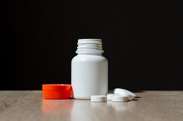 Plastic jar for pills. White jar with orange lid. The sterile container stands on the table. Cold medicine. Pharmaceutical activity. Multi-colored capsules with a medicinal substance.