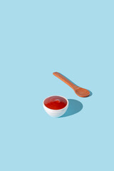 Fresh ketchup in a small white bowl on a pastel blue background. Minimalistic food concept. Creative idea.