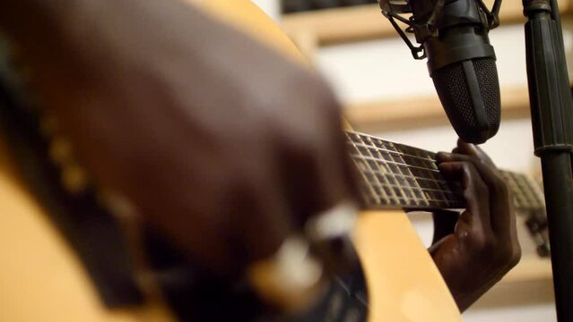 Close shot of black man playing acoustic guitar sitting on chair in recording studio