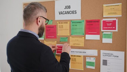 Job center employee pinning job vacancies on employment noticeboard.