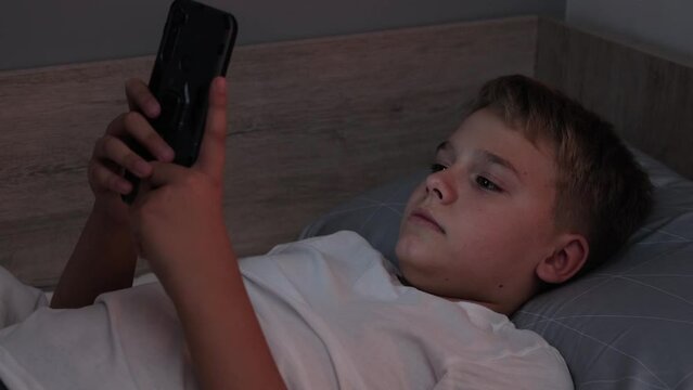 Male teenager lying on his bed while scrolling through social media on his phone