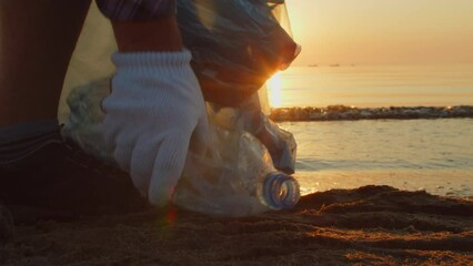 Close-up, a volunteer collects plastic garbage on the beach with gloves and puts it in a garbage bag. Volunteers clean the beach. Cleaning up trash on the beach. - Powered by Adobe