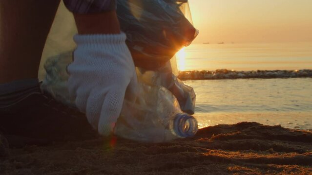 Close-up, a volunteer collects plastic garbage on the beach with gloves and puts it in a garbage bag. Volunteers clean the beach. Cleaning up trash on the beach. 