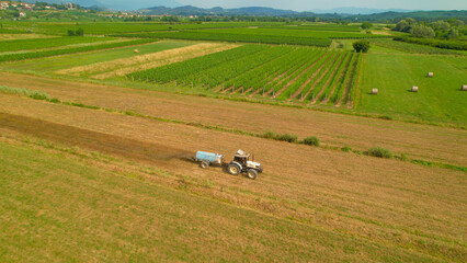 AERIAL: White tractor with slurry spreader fertilizing arable land in autumn - obrazy, fototapety, plakaty