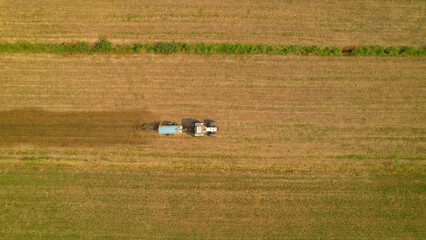 AERIAL, TOP DOWN: Farm tractor spreading manure on arable land in autumn season - obrazy, fototapety, plakaty