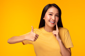 Happy woman take care tooth Give thumb up Young lady has nice smile fresh breath Beautiful asian girl has beautiful tooth, white teeth nice tooth alignment Pretty female show tooth Yellow background - obrazy, fototapety, plakaty