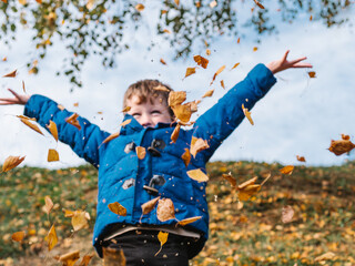 elementary boy happy throwing up yellow leaves and having fun in autumn par