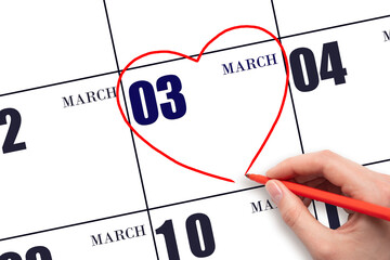 A woman's hand drawing a red heart shape on the calendar date of 3 March. Heart as a symbol of love.