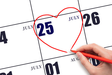 A woman's hand drawing a red heart shape on the calendar date of 25 July. Heart as a symbol of love.