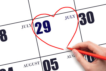 A woman's hand drawing a red heart shape on the calendar date of 29 July. Heart as a symbol of love.
