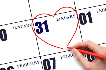 A woman's hand drawing a red heart shape on the calendar date of 31 January. Heart as a symbol of...