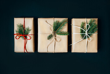 top view of three Christmas gifts in a box decorated with ribbons and a branch of a Christmas tree on a black background - obrazy, fototapety, plakaty